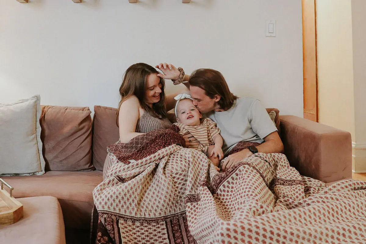 A family of three in New York City are sitting on their couch with a dignify kantha blanket.