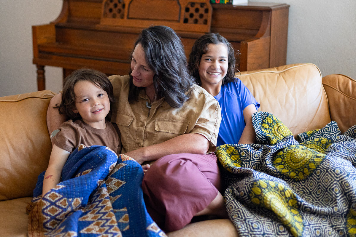 A family is smiling and reading a book together under a colorful handmade kantha throw on the sofa in Erin's San Diego home