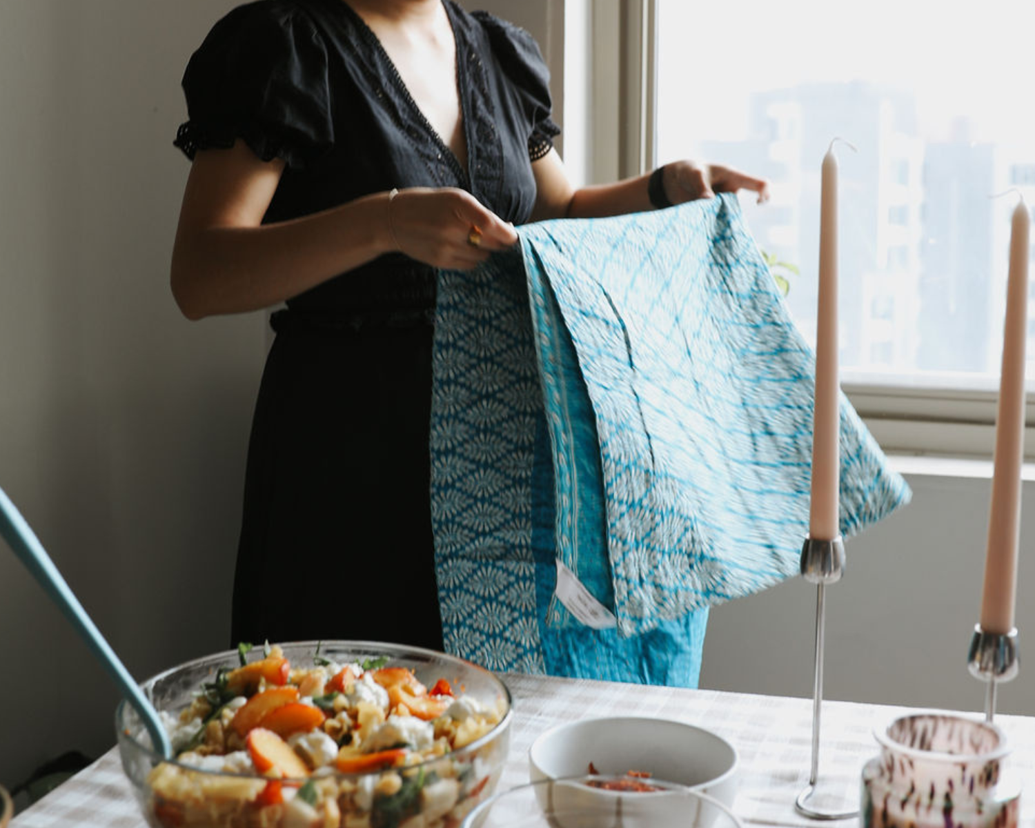 Woman is folding a dignify kantha blanket as she hosts friends at her home for lunch